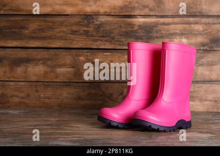 Ein Paar leuchtend pinkfarbene Gummistiefel auf einer Holzfläche. Platz für Text Stockfoto