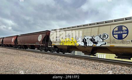 EMPORIA, KANSAS - 8. MÄRZ 2023 Ein BNSF-Güterzug, der Getreidewagen transportiert, die für den Transport von Mais, Weizen und Sojabohnen verwendet wurden, auf denen heute in westlicher Richtung künstlerisches Graffiti gemalt wurde. Stockfoto