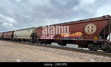 EMPORIA, KANSAS - 8. MÄRZ 2023 Ein BNSF-Güterzug, der Getreidewagen transportiert, die für den Transport von Mais, Weizen und Sojabohnen verwendet wurden, auf denen heute in westlicher Richtung künstlerisches Graffiti gemalt wurde. Stockfoto