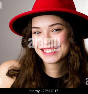 Schönes Teenage-Mädchen mit breiter Krempe, roter Fedora | Lächeln | Headshot | Blickkamera Stockfoto