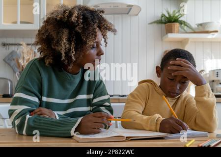 Fokussierte, birassistische Tutorin gibt Privatunterricht, rücksichtsvoller Kinderschüler am Schreibtisch zu Hause Stockfoto