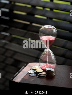 Sand läuft oder fließend von einer Sanduhr mit Münzen daneben. Speicherplatz kopieren. Zeit ist Geld. Stockfoto