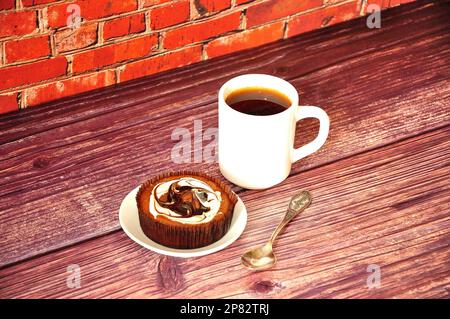 Eine Untertasse mit einer Kekskuchen-Torte in Schokoladencreme und einer Tasse heißem schwarzen Kaffee auf einem Holztisch. Nahaufnahme. Stockfoto