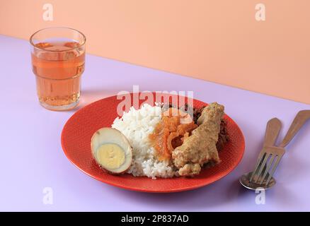 Nasi Gudeg Jogja Komplit mit Opor Ayam Chicken Curyy, Eiern, Jackfrucht-Eintopf und Krecek. Serviert mit Tee auf rotem Teller Stockfoto