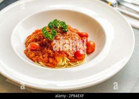 Spaghetti mit Tomatensoße und Schweinehackfleisch. Spaghetti mit Tomatensauce in weißem, wunderschönem Gericht, Tageslicht aus dem Fenster. Stockfoto