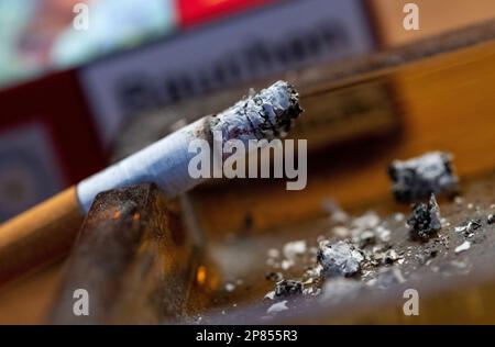 München, Deutschland. 06. März 2023. Ein Zigarettenschweler in einem Aschenbecher auf einem Tisch. Kredit: Sven Hoppe/dpa/Alamy Live News Stockfoto