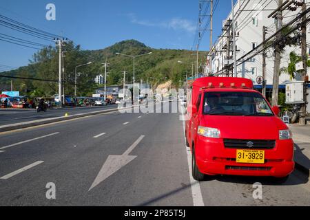 Ein rotes Tuk-tuk, ein Vierrädriges Taxi, befindet sich in der Hauptstraße durch Kamala, die geparkten, grünen Hügeln im b/g; Kamala Beach, Phuket, Thailand Stockfoto