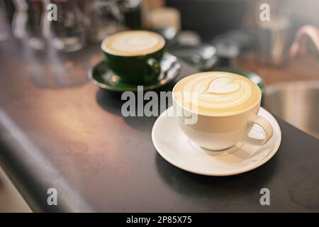 Mit Liebe gemacht. Aus einem hohen Winkel mit zwei Tassen Cappuccino auf einer Arbeitsfläche. Stockfoto