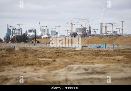 Hamburg, Deutschland. 08. März 2023. Die Silhouette von HafenCity mit der Konzerthalle Elbphilharmonie (l) und ihren zahlreichen Baustellen ist hinter der Sandfüllung zu sehen, um die Baustelle auf Grasbrook im Hafen vorzubereiten. Auf der jährlichen Pressekonferenz der HafenCity Hamburg GmbH wurden die Zukunftsstrategien in den Stadtentwicklungsgebieten Grasbrook, Science City Hamburg Bahrenfeld, Billebogen und HafenCity sowie weitere Themen vorgestellt. Kredit: Christian Charisius/dpa/Alamy Live News Stockfoto