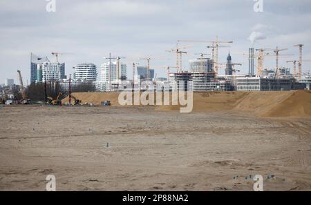 Hamburg, Deutschland. 08. März 2023. Die Silhouette von HafenCity mit der Konzerthalle Elbphilharmonie (l) und ihren zahlreichen Baustellen ist hinter der Sandfüllung zu sehen, um die Baustelle auf Grasbrook im Hafen vorzubereiten. Auf der jährlichen Pressekonferenz der HafenCity Hamburg GmbH wurden die Zukunftsstrategien in den Stadtentwicklungsgebieten Grasbrook, Science City Hamburg Bahrenfeld, Billebogen und HafenCity sowie weitere Themen vorgestellt. Kredit: Christian Charisius/dpa/Alamy Live News Stockfoto