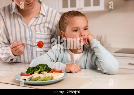 Mutter füttert ihre Tochter in der Küche, Nahaufnahme. Ein kleines Mädchen weigert sich, zu Abend zu essen Stockfoto