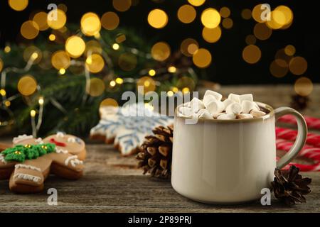 Köstliche heiße Schokolade mit Marshmallows und Weihnachtsdekor auf Holztisch vor verschwommenem Licht, Platz für Text Stockfoto