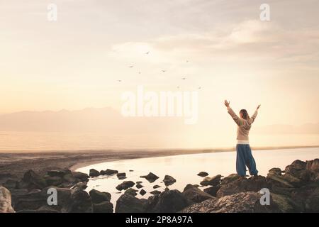 Eine Frau mit ausgestreckten Armen atmet vor einer spektakulären Meereslandschaft ein Stockfoto