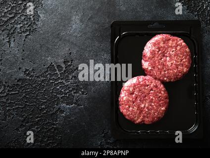 Rohe Hamburger mit Hackfleisch in einer Vakuumschale aus Kunststoff auf schwarzem Steinhintergrund. Draufsicht Stockfoto