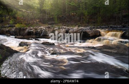 Eine lange Aufnahme eines ruhigen Flusses schlängelt sich durch eine malerische Landschaft mit majestätischen Felsen und üppigen Bäumen Stockfoto