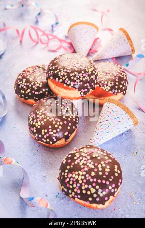 Schokoladen-Berliner-Gebäck für Karneval und Party. Deutsche Krapfen oder Donuts mit Bändern und Konfetti. Farbenfrohes Karneval- oder Geburtstagsbild Stockfoto