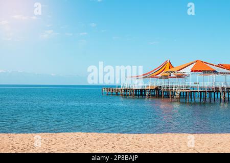 Holzpier mit orange-roter Markise über Meer, See, Meer mit Strand ohne Menschen. Reisen, Urlaub, Sommerhintergrund. Speicherplatz kopieren Stockfoto