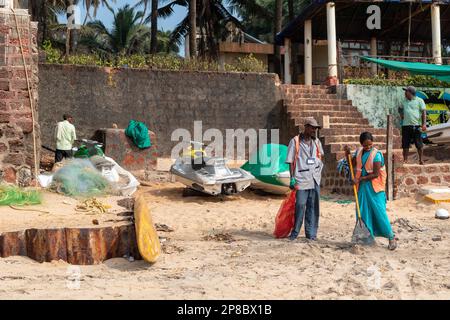 Candolim, Goa, Indien - Januar 2023: Indische Sanitäter säubern den Müll mit Besen am Touristenstrand in Sinquerim. Stockfoto
