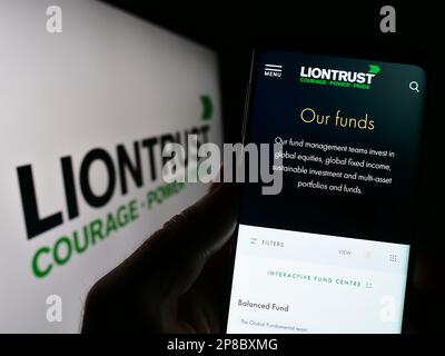 Person mit Smartphone und Webseite des britischen Unternehmens Liontrust Asset Management plc auf dem Bildschirm mit Logo. Konzentrieren Sie sich auf die Mitte des Telefondisplays. Stockfoto
