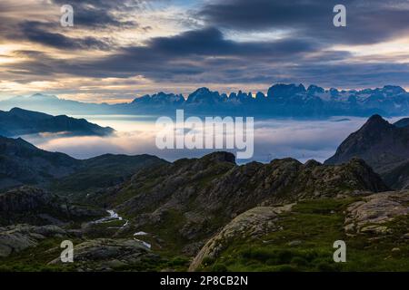 Sonnenaufgang mit Wolkenfluten über dem Campiglio Valley. Blick von den Felsen des Val d'Amola. Im Hintergrund die Profile der Brenta-Dolomiten. Stockfoto