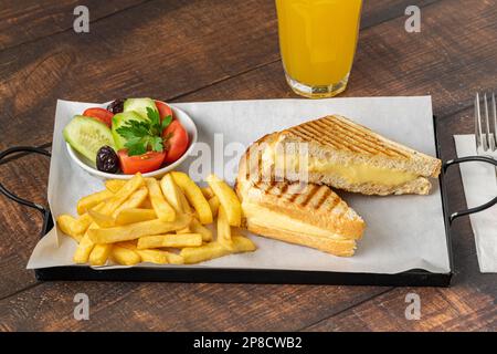 Cheddar-Käse-Toast mit pommes Frites und Salat auf einem Holztisch Stockfoto