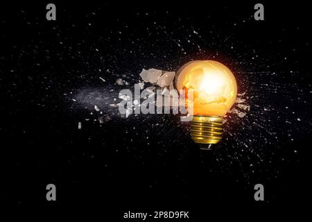 Kleine Glühbirne, die vor schwarzem Hintergrund explodiert Stockfoto