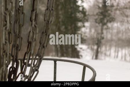 Nahaufnahme eines Disc-Golfkorbs in einem verschneiten Wald in Nordfrankreich Stockfoto