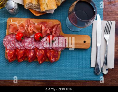 Spanische leckere Gerichte, die Würstchen und Schinken mit Tomaten am Holzschreibtisch schneiden Stockfoto