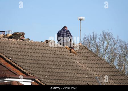 Ein Dachdecker, der Kammfliesen auf dem Dach eines Hauses repariert Stockfoto