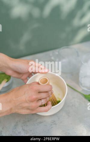 Blick von oben auf eine Frau, die mit einem Schneebesen ein gefrorenes Matcha-Getränk zubereitet Stockfoto