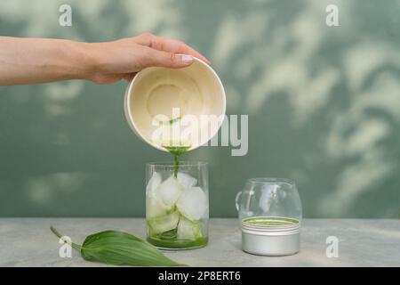 Nahaufnahme einer Frau, die gequisselten Matcha-Tee in ein Glas gefüllt mit Eiswürfeln gießt Stockfoto