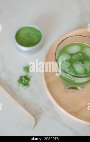 Blick von oben auf ein Glas gefrorenes Matcha-Getränk, Matcha-Pulver und Matcha-Löffel Stockfoto