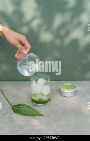 Nahaufnahme einer Frau, die Wasser in ein Glas gießt, um ein gefrorenes Matcha-Getränk herzustellen Stockfoto