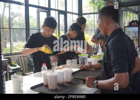Der Barkeeper in einem Café gießt Milch und Soße ein, während der Kellner vor ihm wartet Stockfoto