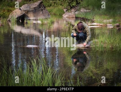Eine Frau, die auf einem Felsen hockt und ins Wasser blickt: Lake Lemolo, Oregon, USA Stockfoto