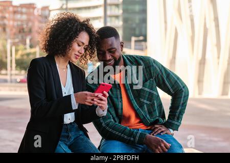 Multiethnisches Paar, das ein mobiles Außenleben in der Stadt nutzt Stockfoto