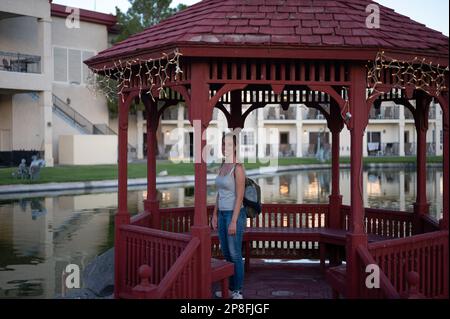 Ein junges Mädchen sitzt in dem kleinen roten Holzpavillon im japanischen Stil, der den Teich schmückt. Stockfoto