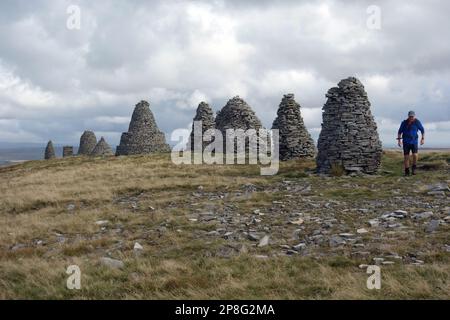 Ein Mann, der am Stone Cairns auf dem Summit of „Nine Standards Rigg“ in der Nähe von Hartley auf dem Coast to Coast Path im Yorkshire Dales National Park vorbeigeht. Stockfoto