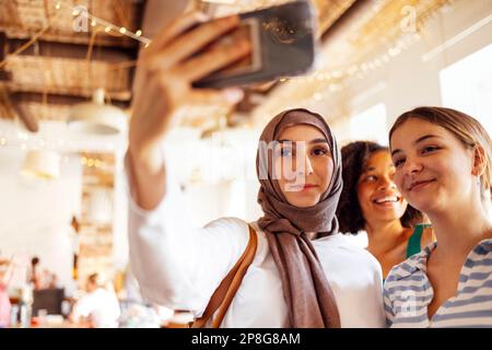 Drei süße Mädchen verschiedener Nationalitäten machen ein Selfie. Weiße, afroamerikanische und muslimische Teenager machen ein Foto von sich selbst. Stockfoto