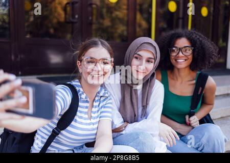 Drei süße Mädchen verschiedener Nationalitäten machen ein Selfie. Weiße, afroamerikanische und muslimische Teenager machen ein Foto von sich selbst. Stockfoto