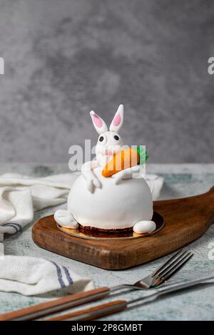 Speziell entworfener Kuchen in Hasenform. Kuchen auf grauem Holztisch und Osterhase Stockfoto
