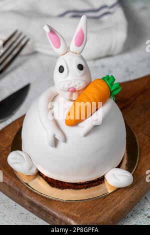 Speziell entworfener Kuchen in Hasenform. Kuchen auf grauem Holztisch und Osterhase Stockfoto