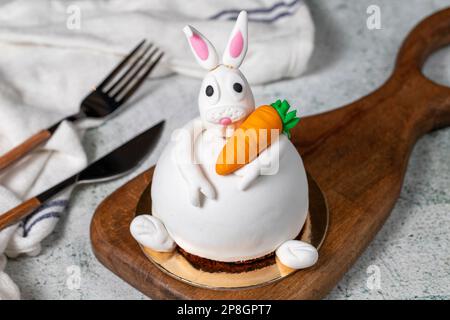 Speziell entworfener Kuchen in Hasenform. Kuchen auf grauem Holztisch und Osterhase Stockfoto