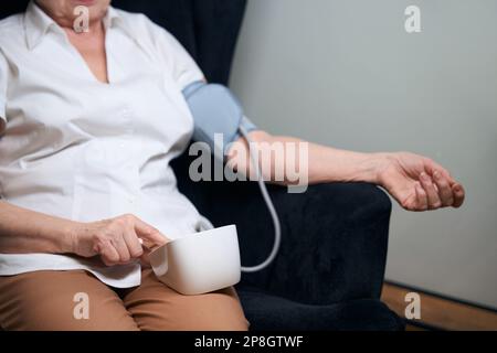 Eine einsame alte Frau sitzt im Stuhl und misst ihren Blutdruck Stockfoto