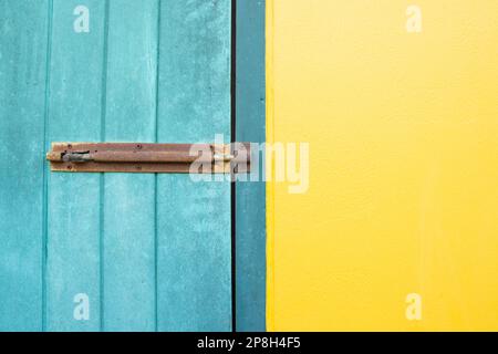 Geschlossenes Vorhängeschloss hängt an den gelben und blauen Wandtüren. Stockfoto