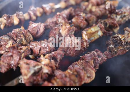 Nahaufnahme mehrerer Spieße mit gegrilltem saftigem Fleisch in Rauch. Stockfoto