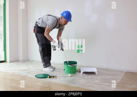 Männlicher Dekorator mischt Farbe im Eimer mit dem Mischer. Stockfoto