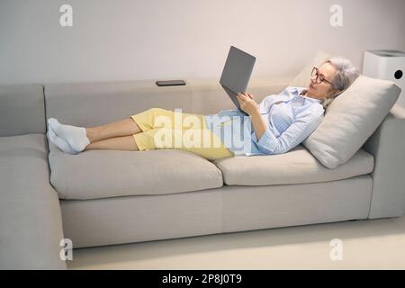 Ein ruhiger Rentner liegt zu Hause mit einem Laptop auf der Couch Stockfoto