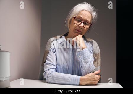Traurige ältere Dame sitzt allein an einem Tisch Stockfoto