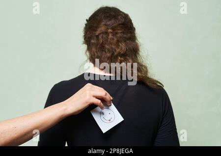 Gekürzte Aufnahme einer Frau, die einen Zettel mit dem Schriftzug vom april-Narren-Tag auf dem Rücken einer anderen Frau schreibt, aprilscherz-Tageskonzept Stockfoto